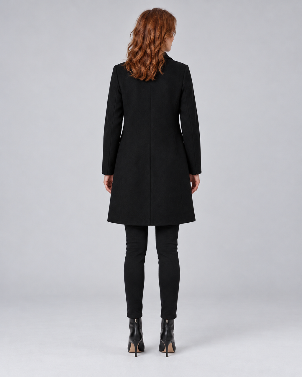 Woman wearing black tailored longline wool-blend coat with button front and side pockets, rear view
