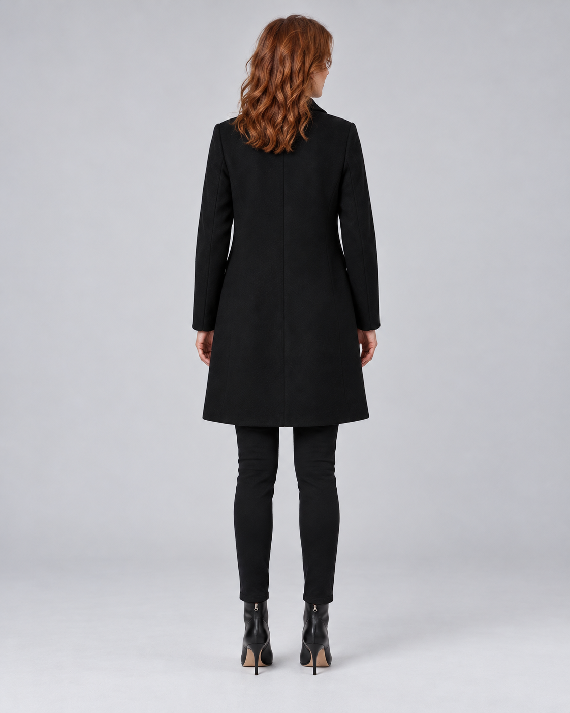 Woman wearing black tailored longline wool-blend coat with button front and side pockets, rear view