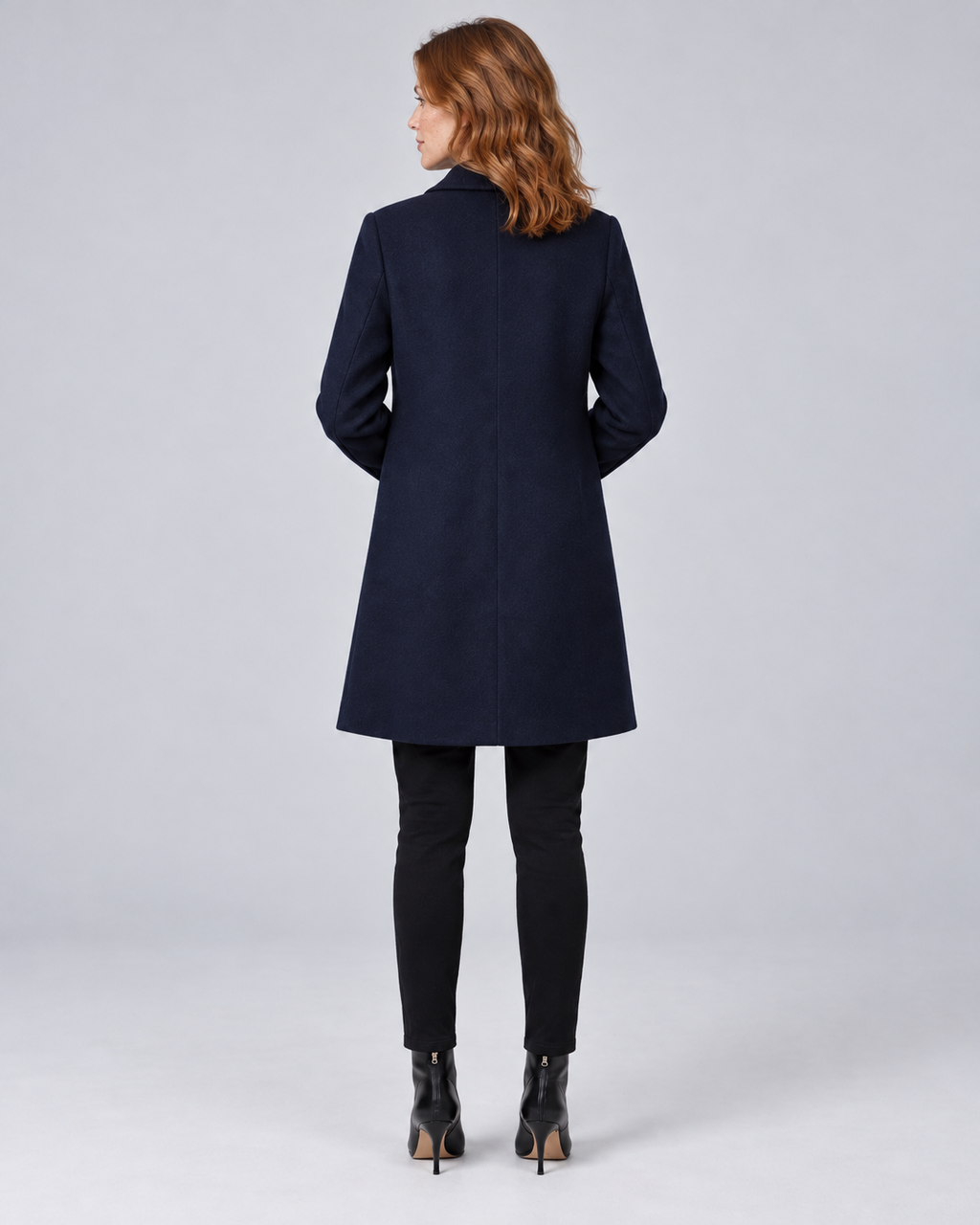 Woman wearing navy tailored longline wool-blend coat with button front and side pockets, rear view
